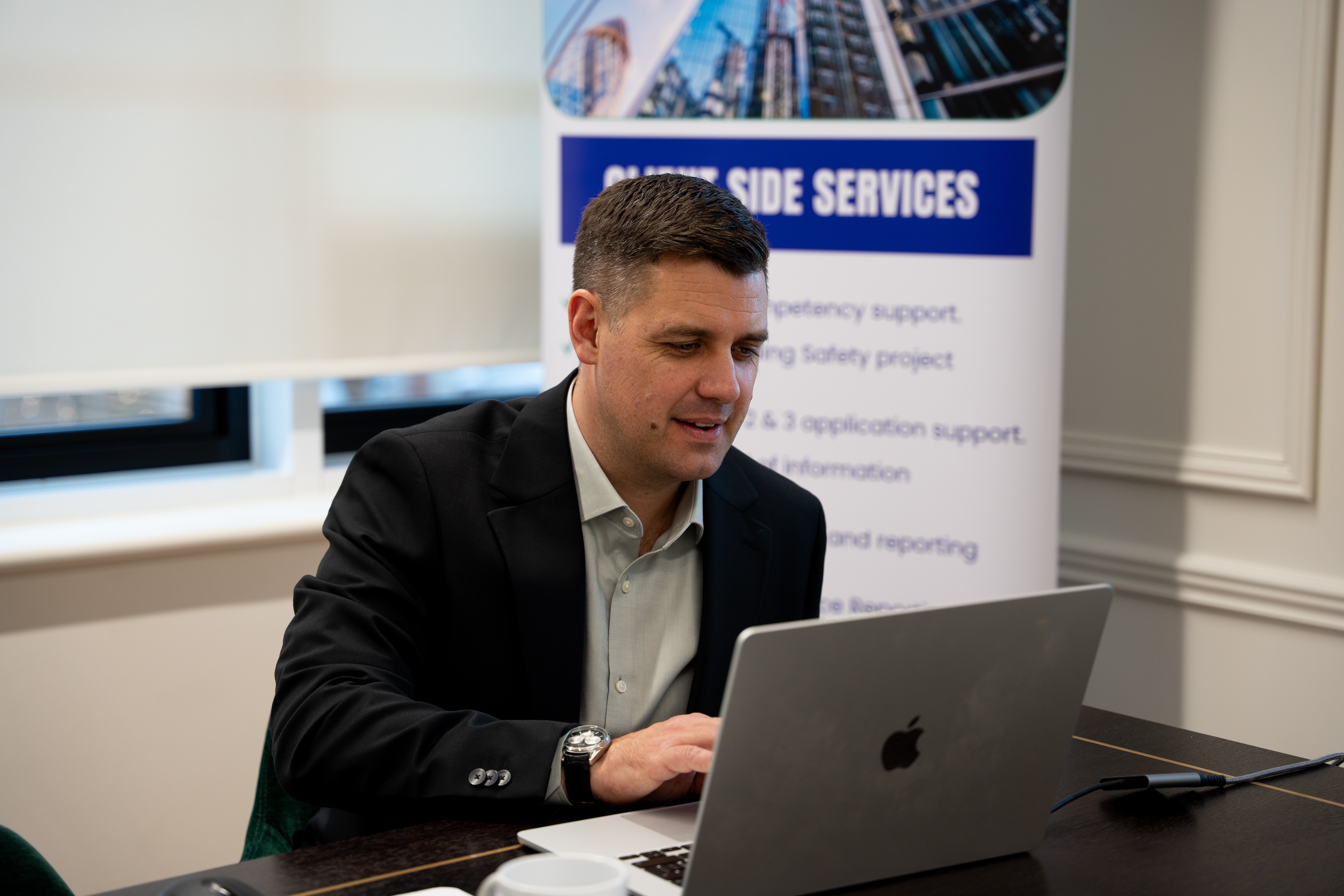 A professional consultant working on a laptop in an office, with a Client Side Services banner in the background.